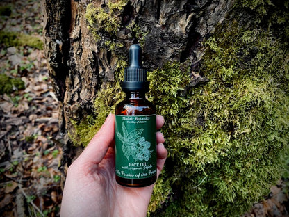 Bottle of Face Oil held in front of a tree with moss