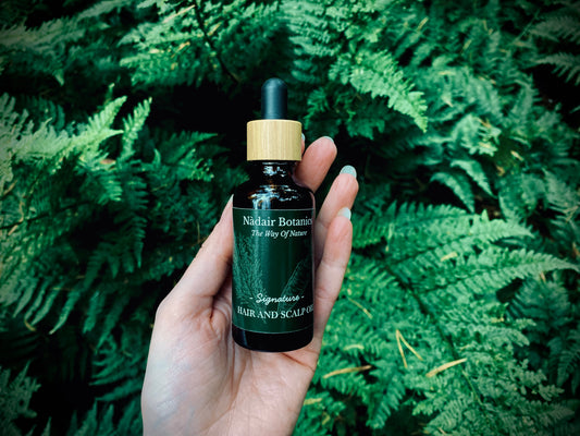 Hand holding a bottle of 'Nair Botanica' product against a green leafy background